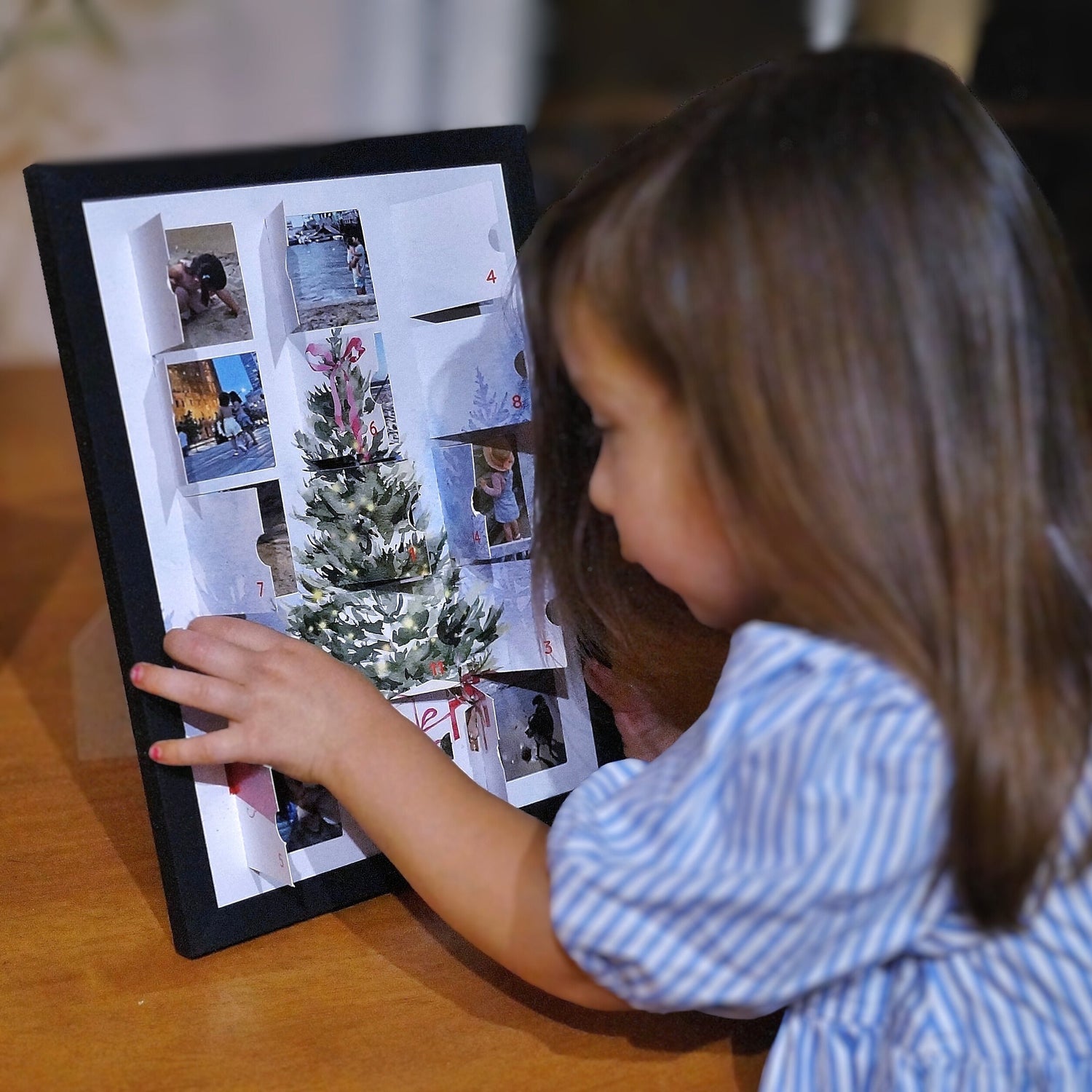 Child interacting with a personalized photo advent calendar in frame displaying Christmas-themed images.