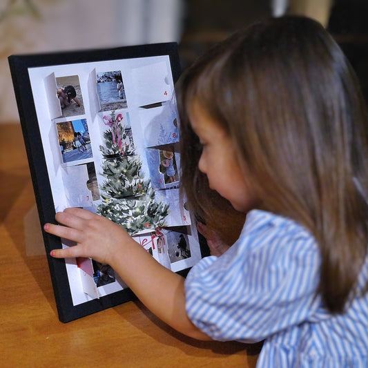 Child interacting with a personalized photo advent calendar in frame displaying Christmas-themed images.